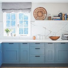 Kitchen with blue cabinets underneath a white worktop and white marble walls
