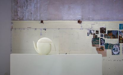 Image of a pale yellow porcelain pot/Jug on display with some imagery on the wall behind 