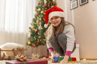 A young girl wearing a Santa hat and playing with a toy in front of a Christmas tree