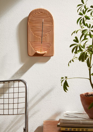 textured incense holder mounted on the wall alongside a plant and other decor bits