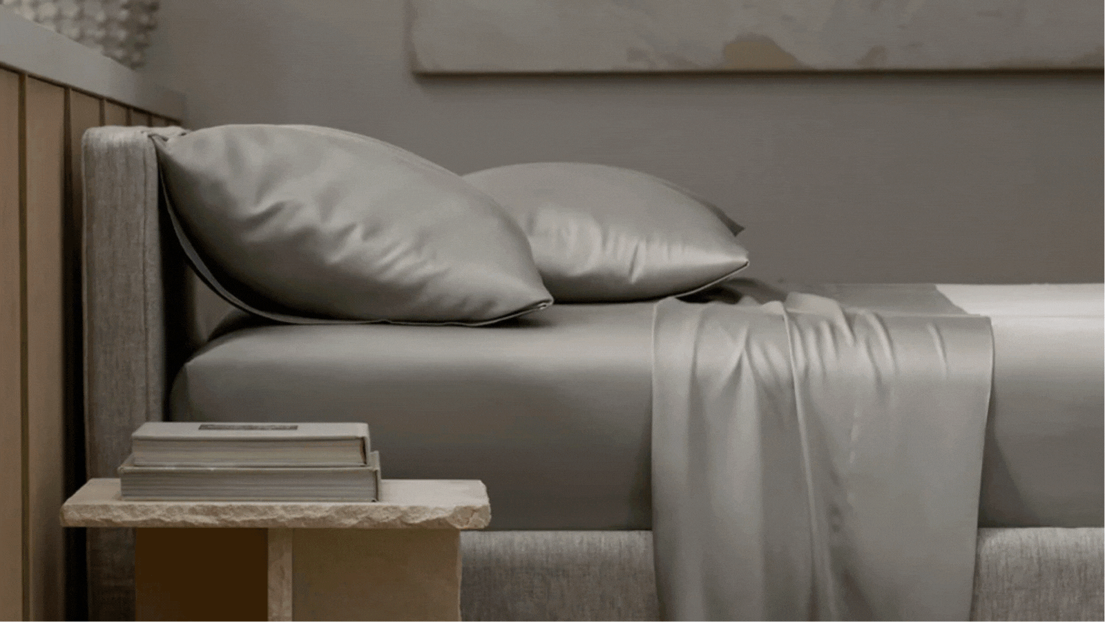 a gif of cozy earth products including a yellow candle on a side table next to a vase, bamboo silk sheets made on a bed with matching pillowcase, blue and gray bedding layered together, and a stack of hand towels on a marble vanity next to a vase of flowers and hand soap and scrubbing brush