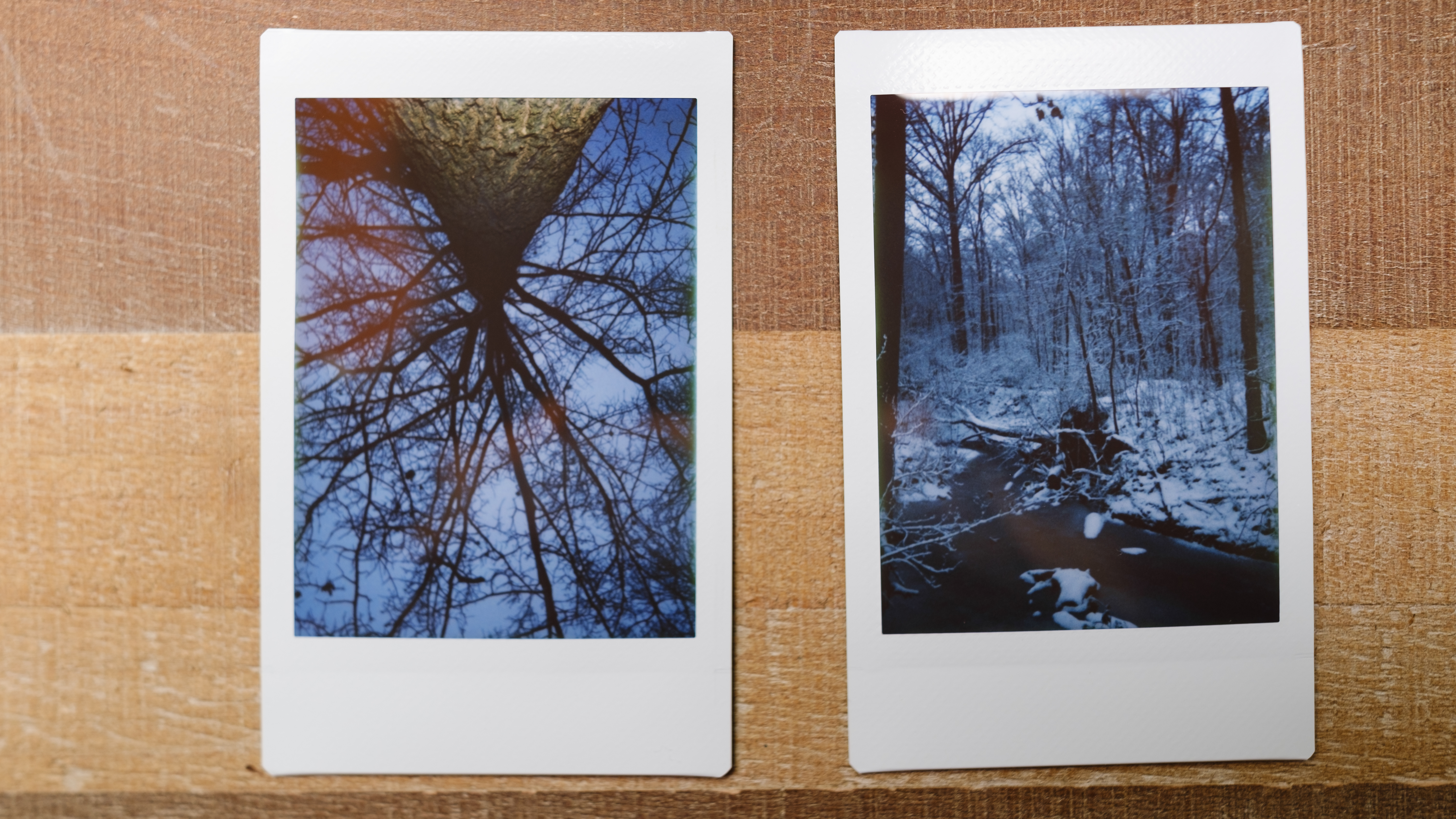 Two images from the Instax Mini SE sit on a table, one is a snowy tree looking up the other is a snowy creek