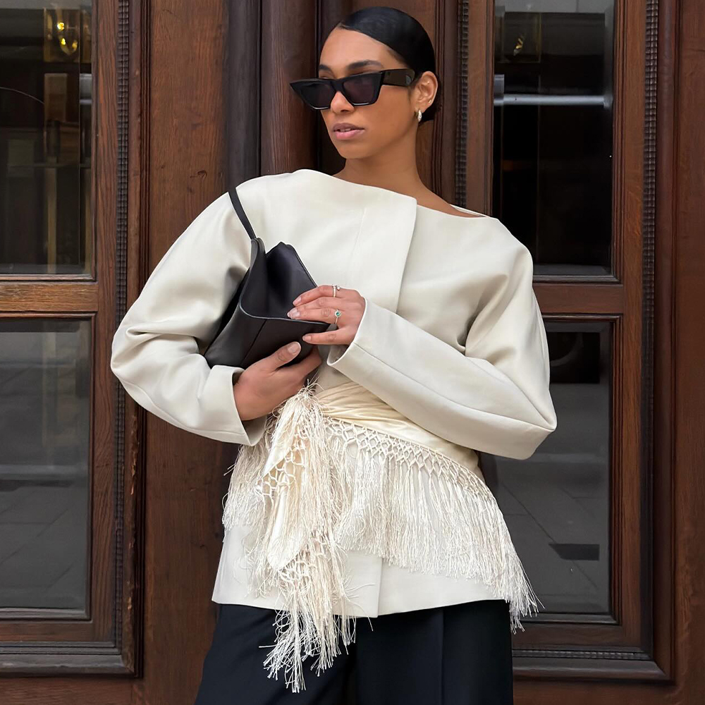 @cherifaakili wearing a cream fringe scarf with a waisted blazer, black trousers, shoulder bag and sunglasses 