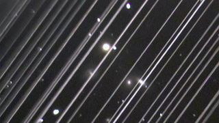 an image of the night sky marked by two dozen diagonal white lines, caused by the movement of satellites