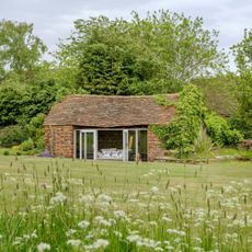 A cottage surrounded by long grass and meadow flowers