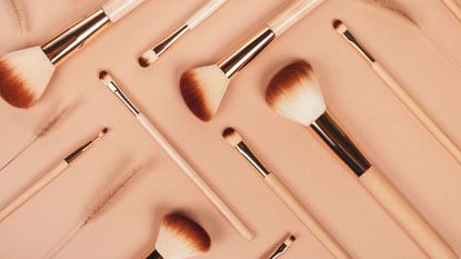 A collection of makeup brushes on a beige background