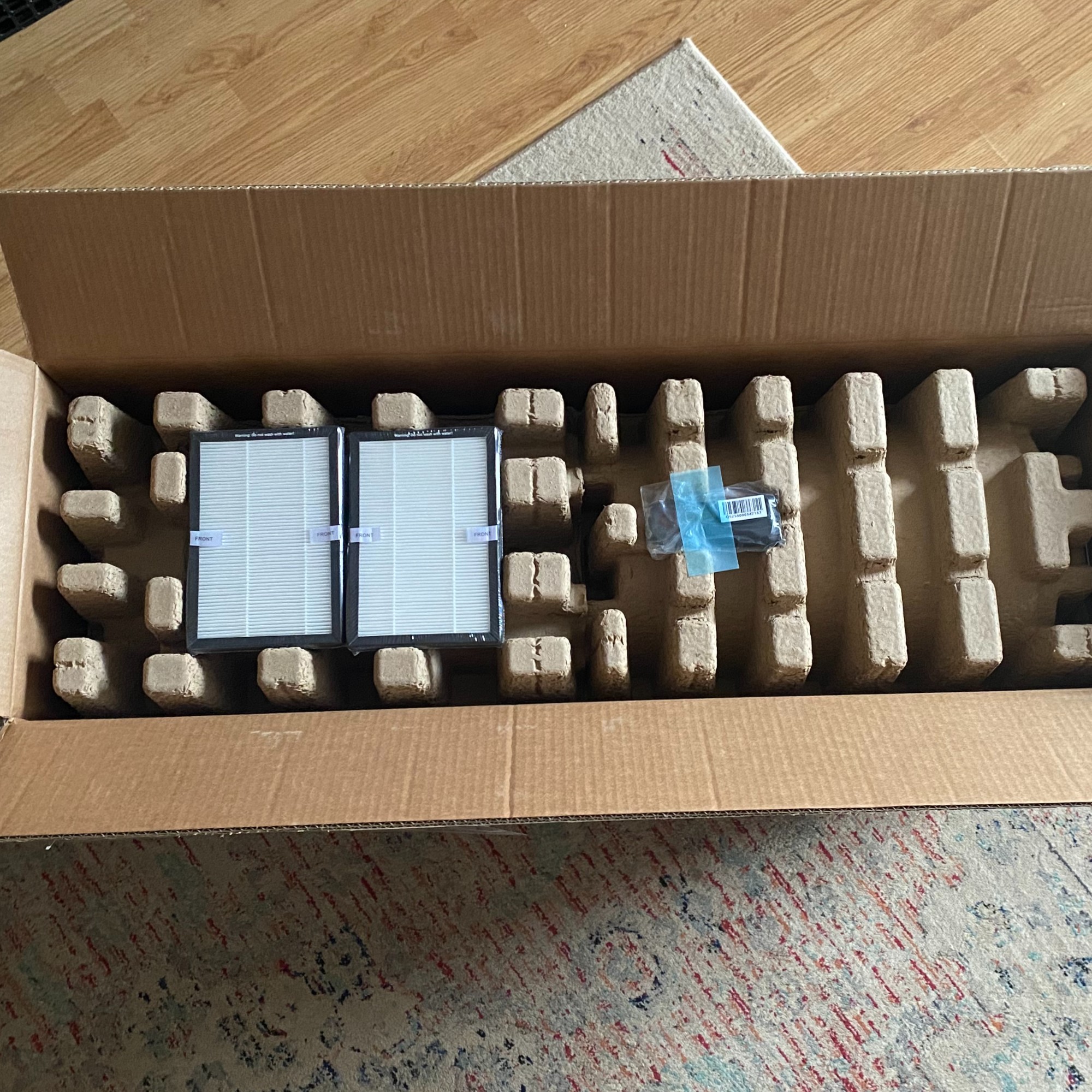 cardboard packaging of the Russell Hobbs RHBLDL25 Bladeless Fan Heater, with two filters and remote control taped to the top