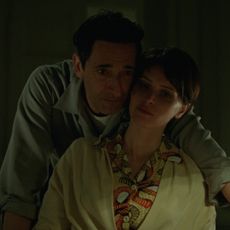 adrien brody leans over felicity jones as they look over blue prints in a still from the brutalist