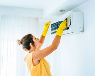 woman wearing gloves to change the filters in an air conditioning unit