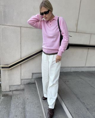 Woman wears a pink polo sweater, baggy white trousers, Bally Boat shoes and wraparound sunglasses.