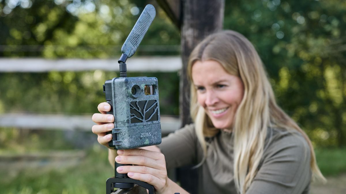 an individual setting up the Zeiss Secacam 3 outdoors on a fence with green hedge row behind them