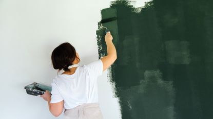 Woman painting white wall green using a roller