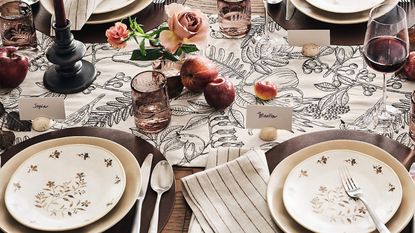 Fall table with cream floral plates, black and white floral runner, and a centerpiece of roses and apples