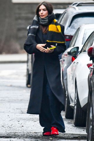 Emily Ratajkowski wearing a black coat, black pants, and red sneakers.