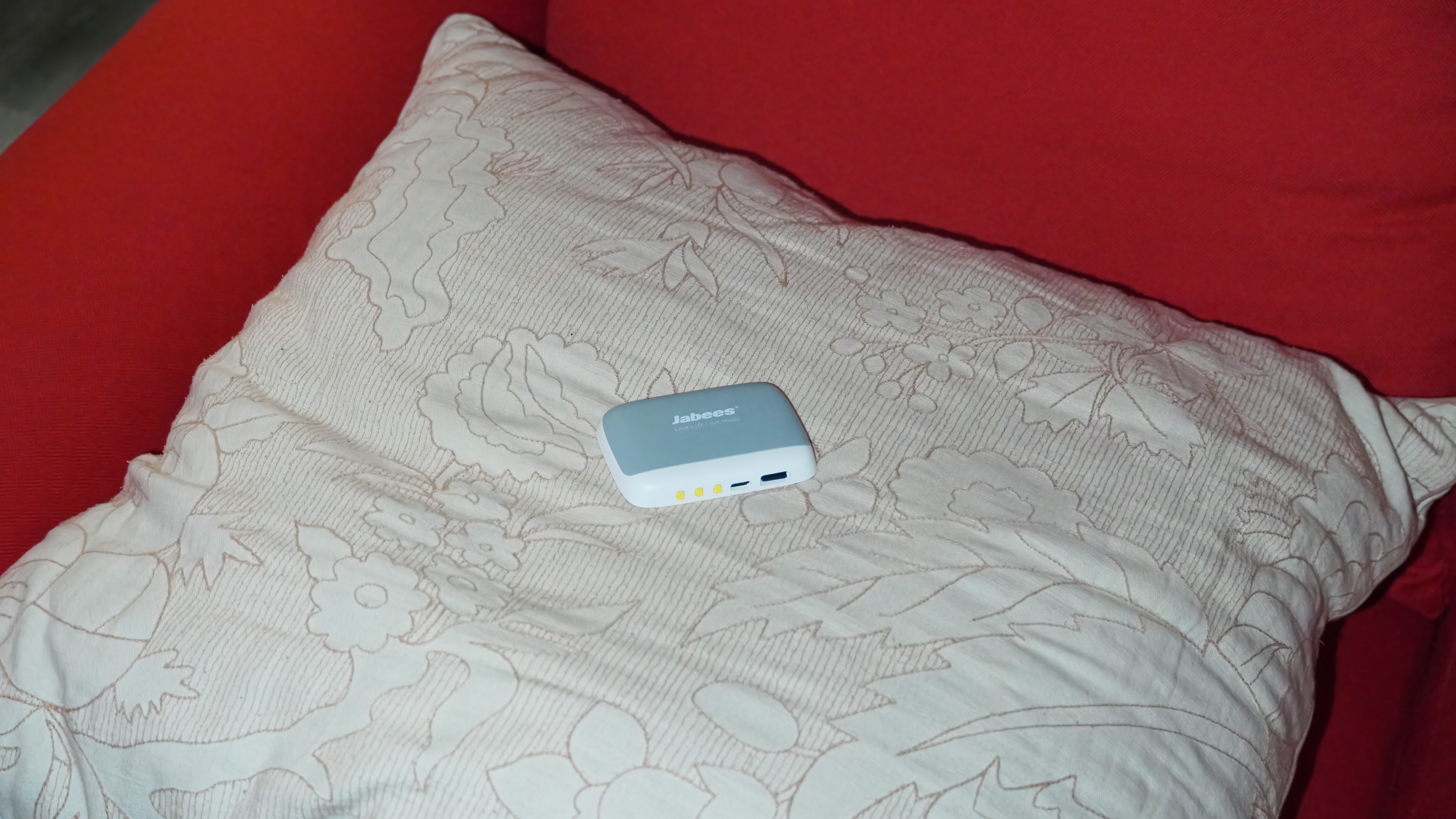 Το Jabees Peace Pillow Speaker στο χέρι και σε ένα μαξιλάρι.