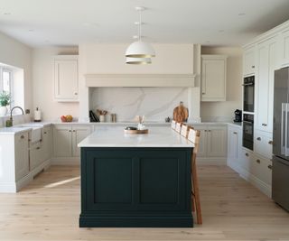 large kitchen with dark green island base topped with white surface, kitchen units in off white and cream walls