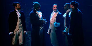 Hamilton cast standing on stage in dim light