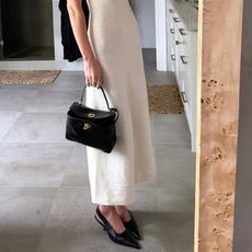 coco wears white dress, black sling backs, and black handbag