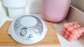 A Homedics white noise machine on a nightstand next to pink accessories