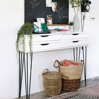 White console table decorated, jute storage baskets underneath, blackboard above table on wall