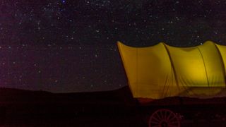 A Conestoga wagon illuminated at night under the stars in Utah