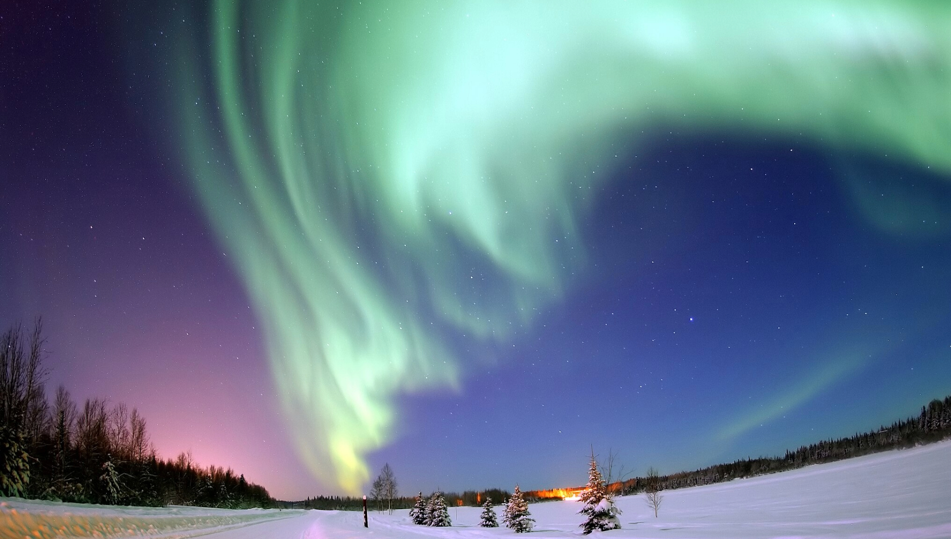 A series of green northern lights illuminate the night sky in snowy Alaska