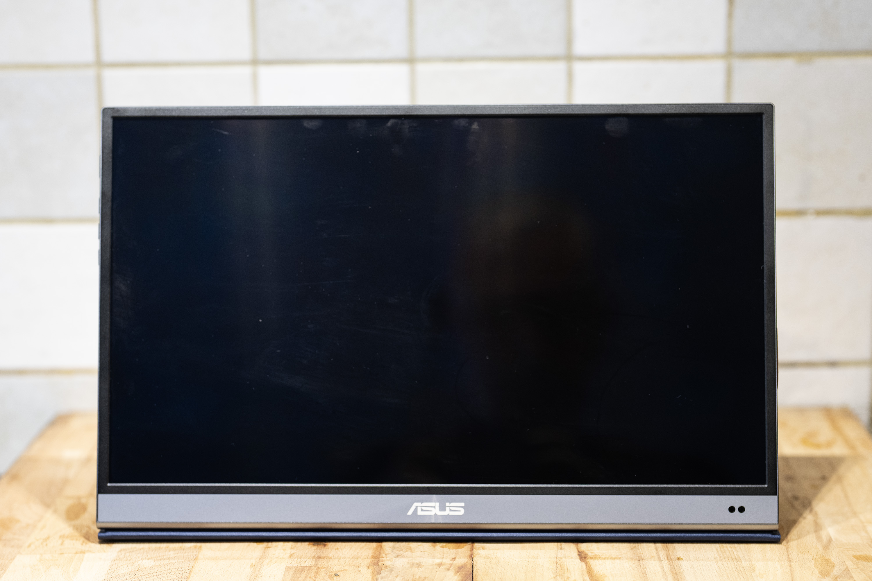 A black and silver ASUS ZenScreen MQ16AH portable monitor on a wooden brown desk