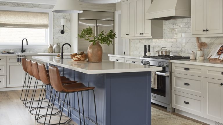 A large kitchen with navy island, greige cabinets and marble wall tiles