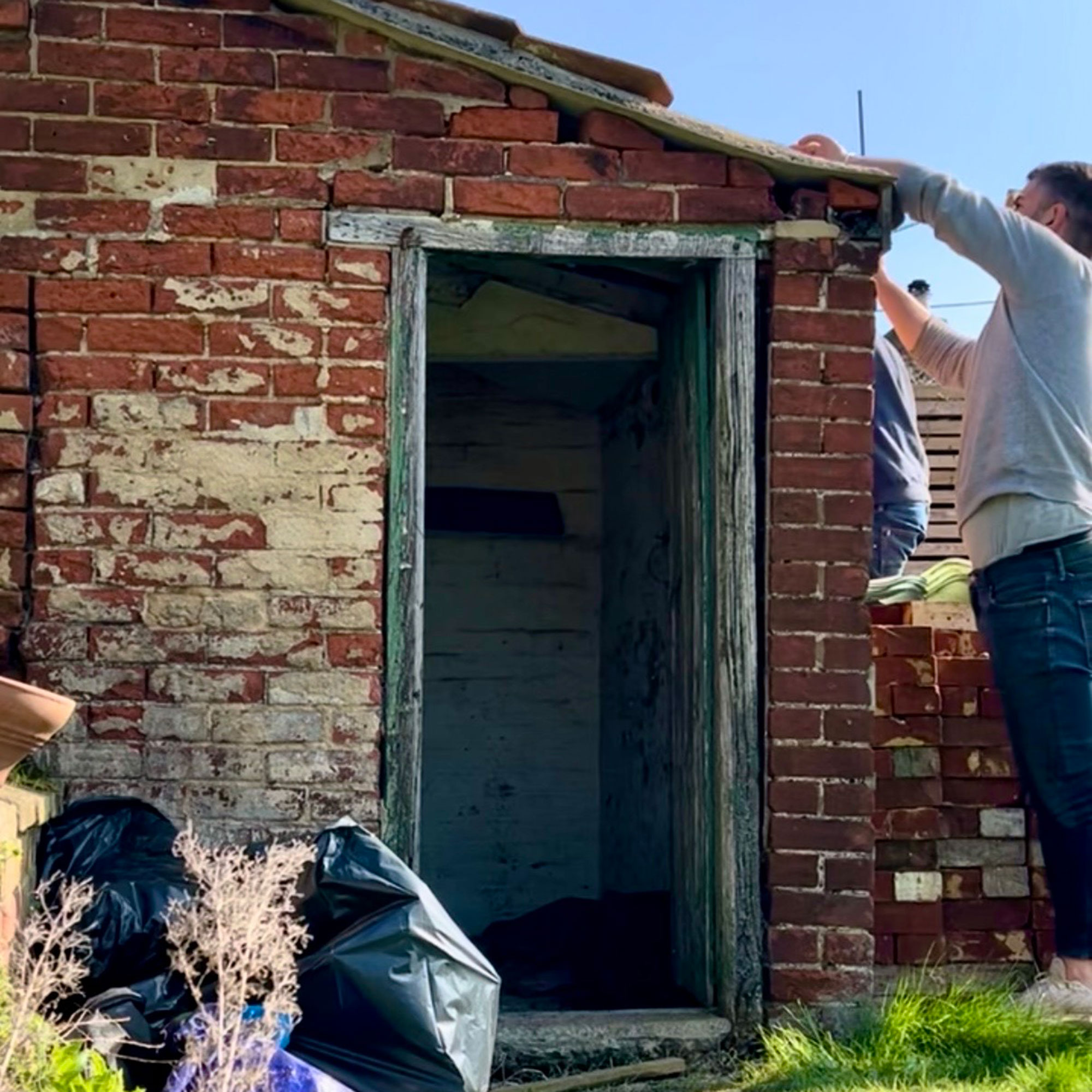 Man tiling roof of brick outhouse with weathered worn down door frame