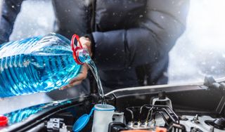 male driver pours antifreeze into the tank to spray the windshield during a snowstorm