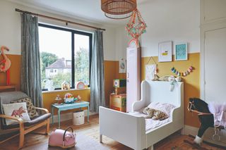Lea-Wilson house: kid's room with yellow and white colourblock walls, white bed with high sides, grey armchair, blue desk and rattan ceiling light