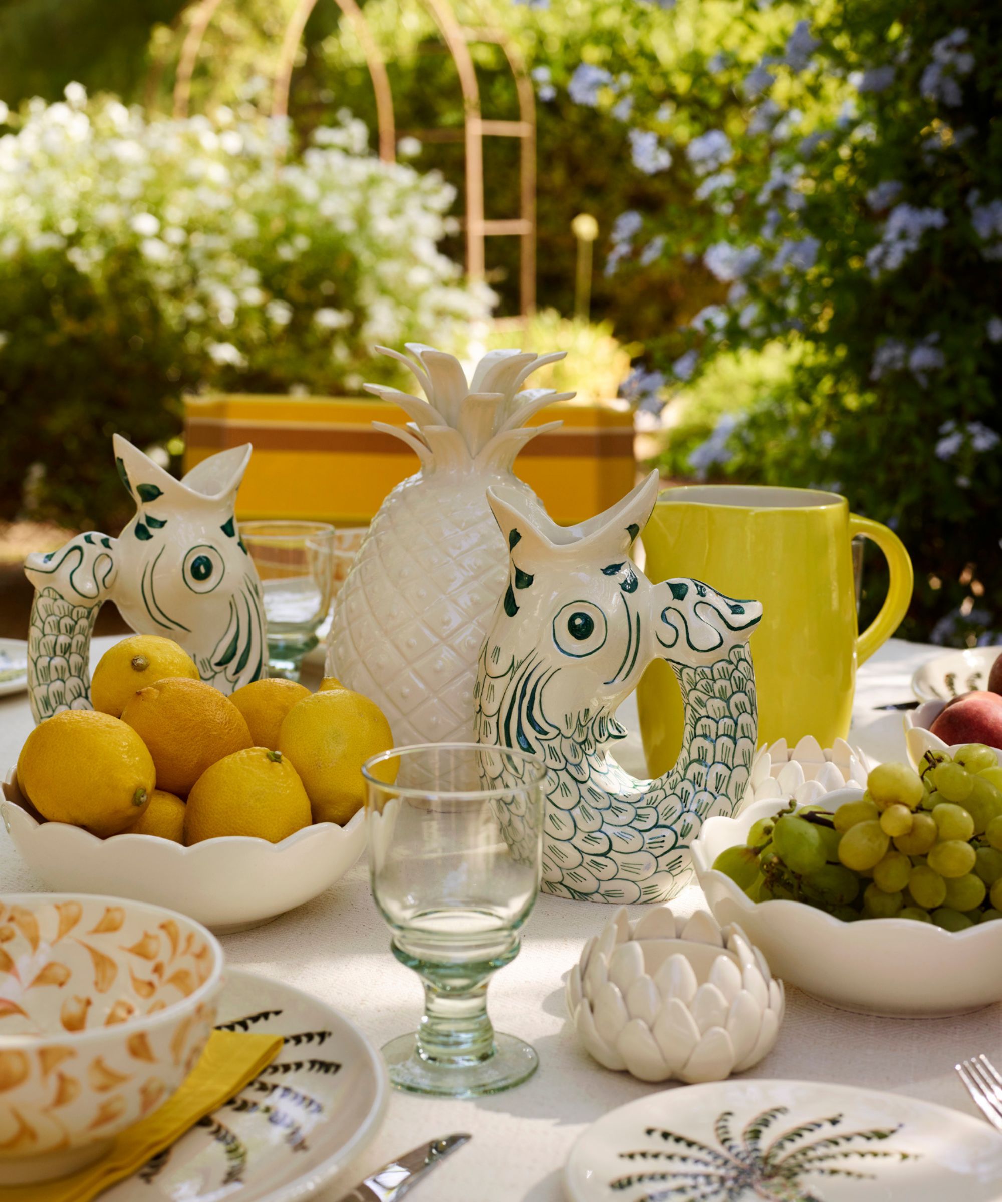Mediterranean themed outdoor dinner party table with fish jugs, a pineapple centerpiece, bowl of lemons and palm tree plates