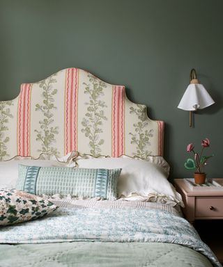 green bedroom with pretty stripe upholsered headboard, pattern bedcover and wall light