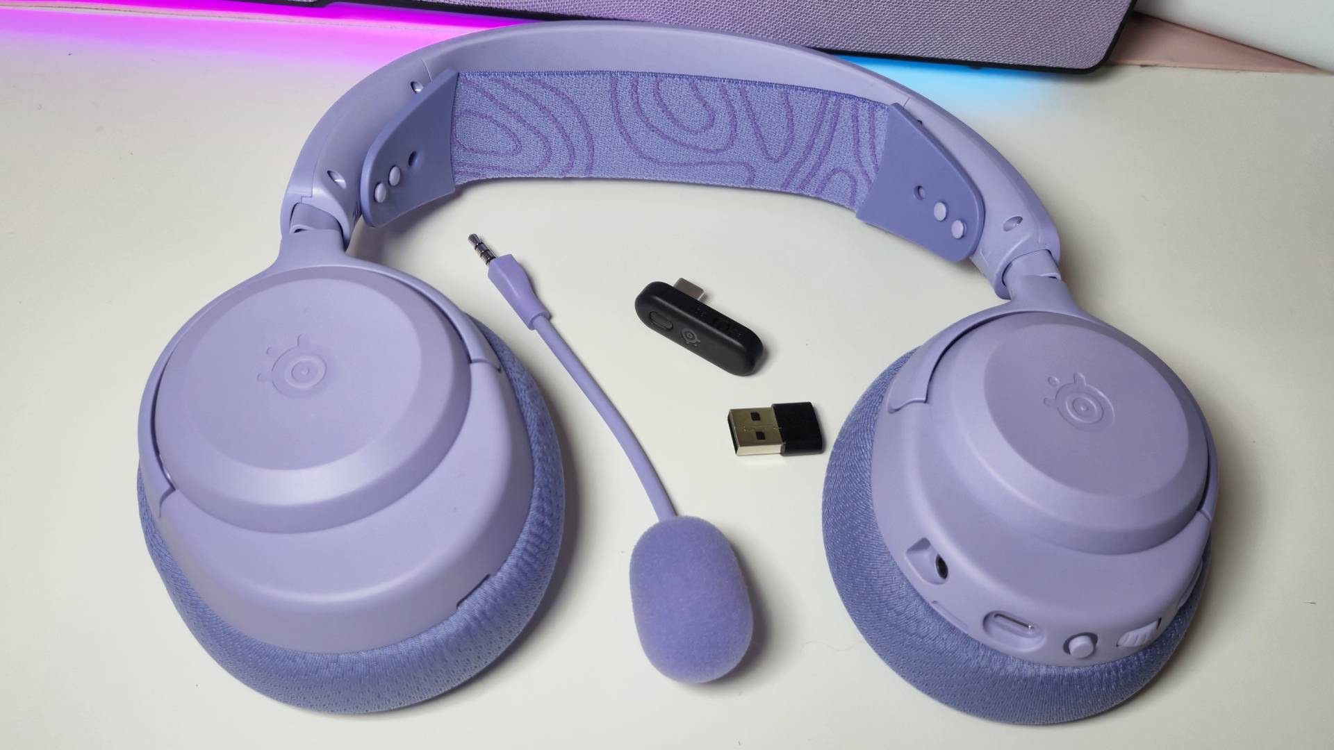 Photos of the SteelSeries Arctis Nova 3 Wireless gaming headset in Lavender, taken by writer Rosalie Newcombe, on a white desk.