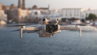 DJI Mini 4 Pro in flight at golden hour with ocean and seaside town in the background