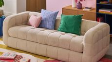 beige La Redoute sofa with three cushions on it, with colorful rug and timber console behind it decorated with a vase and lamp