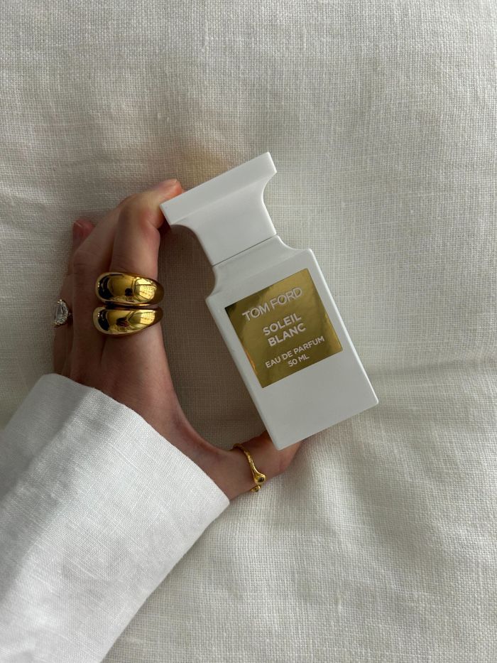 Junior beauty editor Grace Lindsay holding the Tom Ford Soleil Blanc perfume on a linen background