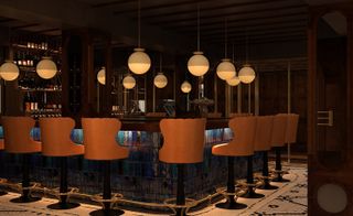 A bar with a dark wood top, blue tiles on the side, light wood bar chairs, wood and glass liquor cabinet and many round pendant lights.