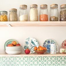 Bowl of apples, a pomegranate and bowl of oranges on a shelf.