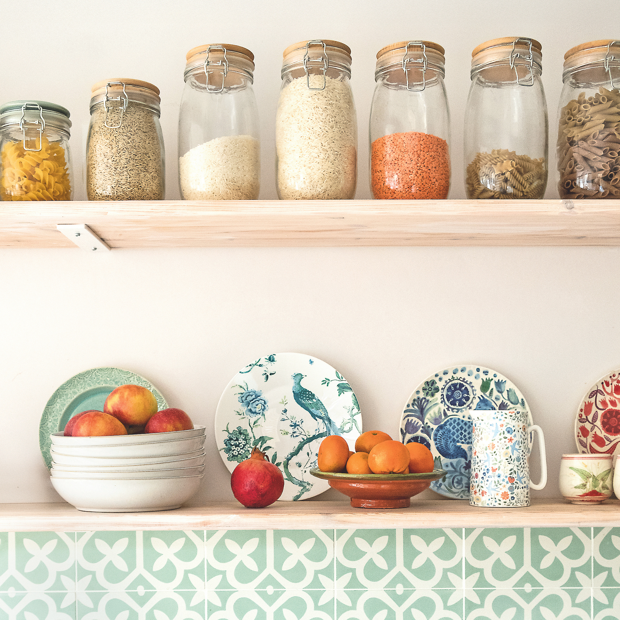 Bowl of apples, a pomegranate and bowl of oranges on a shelf.