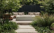 A backyard with concrete firepit and wooden furniture