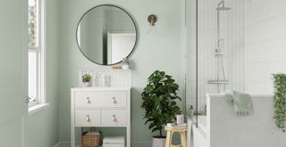 soft green bathroom with white furniture and circular mirror above the sink to show a key bathroom trend 2023