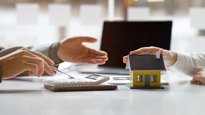 Mortgage borrowing illustration. A person with papers on a desk in front of them and a small model house