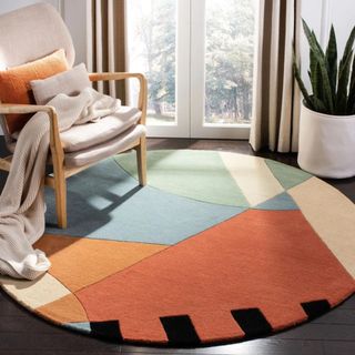 An abstract round rug in orange, blue, green, and white sits on the floor by a wooden chair