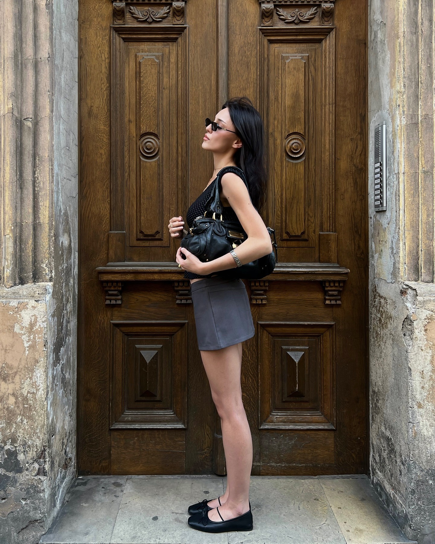 Woman wears black top, grey skirt and ballet flats