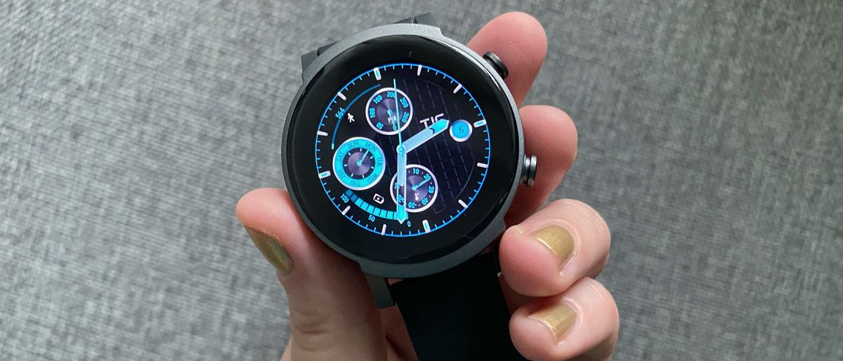 Woman&#039;s hand holding TicWatch E3, with an analog-style watch face