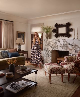 interior designer heidi caillier portait stood in an eclectic living room with a large marble fireplace and mismatched vintage furniture sat on a rug from her loloi rugs collab