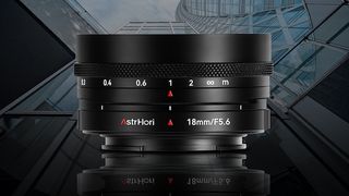 Close-up of an AstrHori 18mm F5.6 camera lens, featuring focus scale and glossy surface, set against a modern glass building background