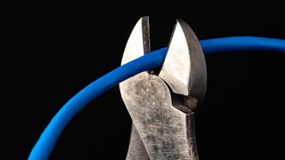 Pliers cut a blue cable against a black background.