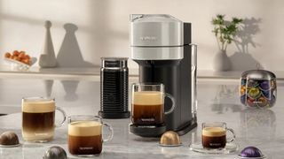 En Nespresso Vertuo Next er omgivet af kaffekapsler på et lyst bord.